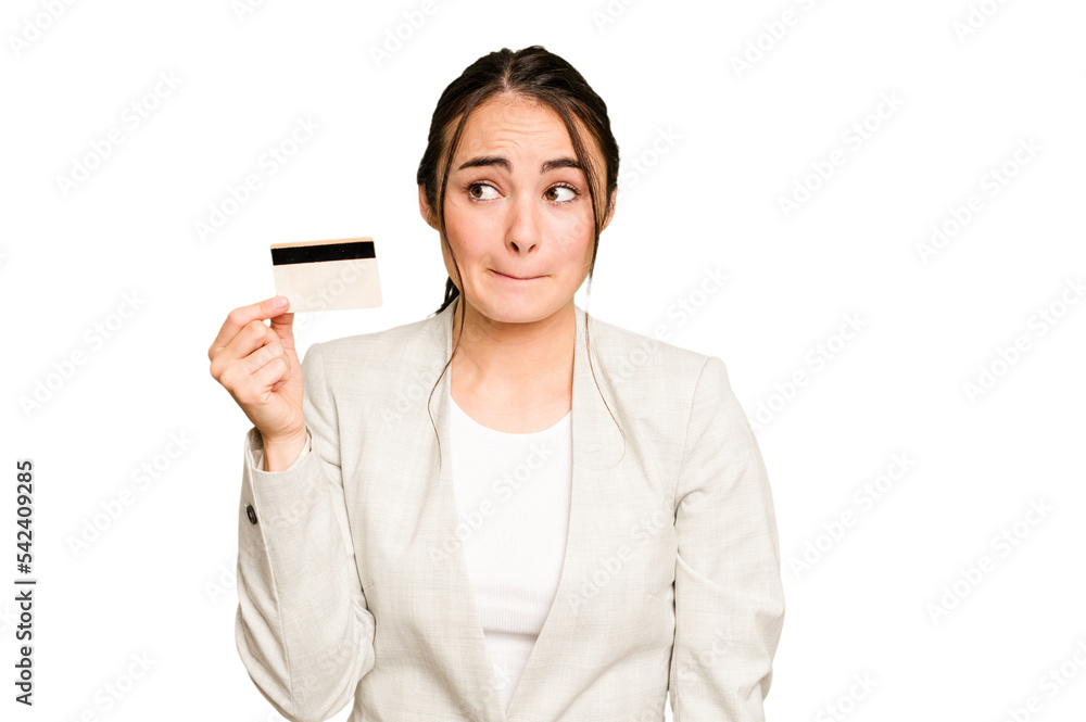 Young caucasian woman holding a credit card isolated on green chroma background confused, feels doubtful and unsure. Young caucasian woman holding a credit card isolated on green chroma background confused, feels doubtful and unsure.
