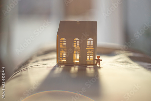 A small paper human showing a white tea light house illuminated by back Sun light