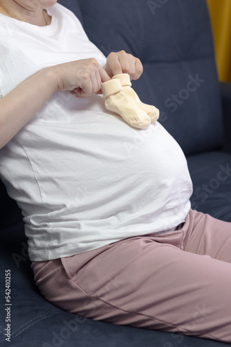 Cute pregnant woman holding socks for newborn. Baby socks on the belly of a pregnant woman