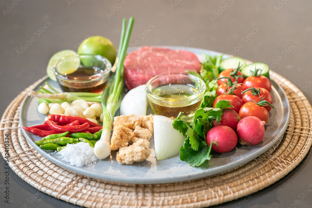 The uncooked ingredients prepared for making yum steak, spicy Thai salad style, are arranged and placed on a local tray set.