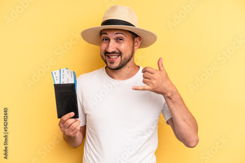 Young latin man holding a flight tickets for vacations showing a mobile phone call gesture with fingers.