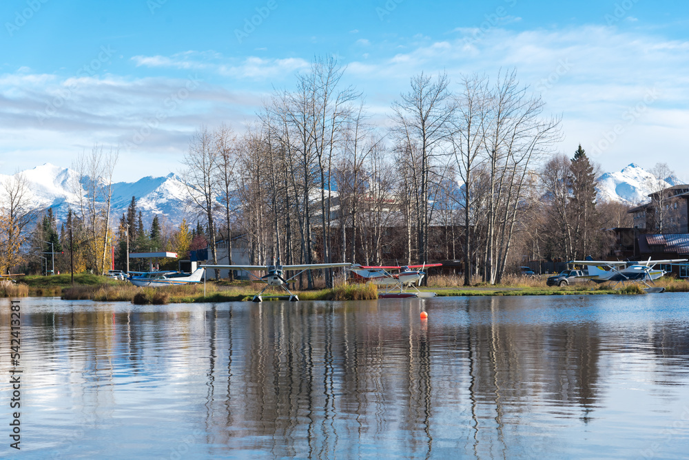 Seaplanes at the base on Lake Spenard with snow cap Chugach Mountain and row of dormant trees in early fall in Anchorage, Alaska Seaplanes at the base on Lake Spenard with snow cap Chugach Mountain and row of dormant trees in early fall in Anchorage, Alaska