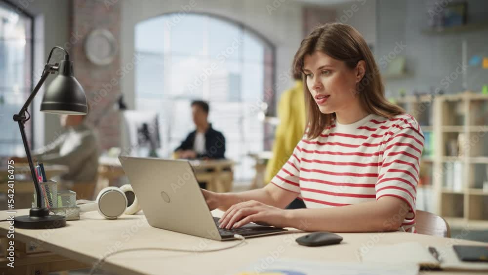 Portrait of White Focused Woman Using Laptop in a Contemporary Spacious Office. Account Specialist Smiling While Having Productive Day. Active Colleagues Working on Computers in the Background. Portrait of White Focused Woman Using Laptop in a Contemporary Spacious Office. Account Specialist Smiling While Having Productive Day. Active Colleagues Working on Computers in the Background.
