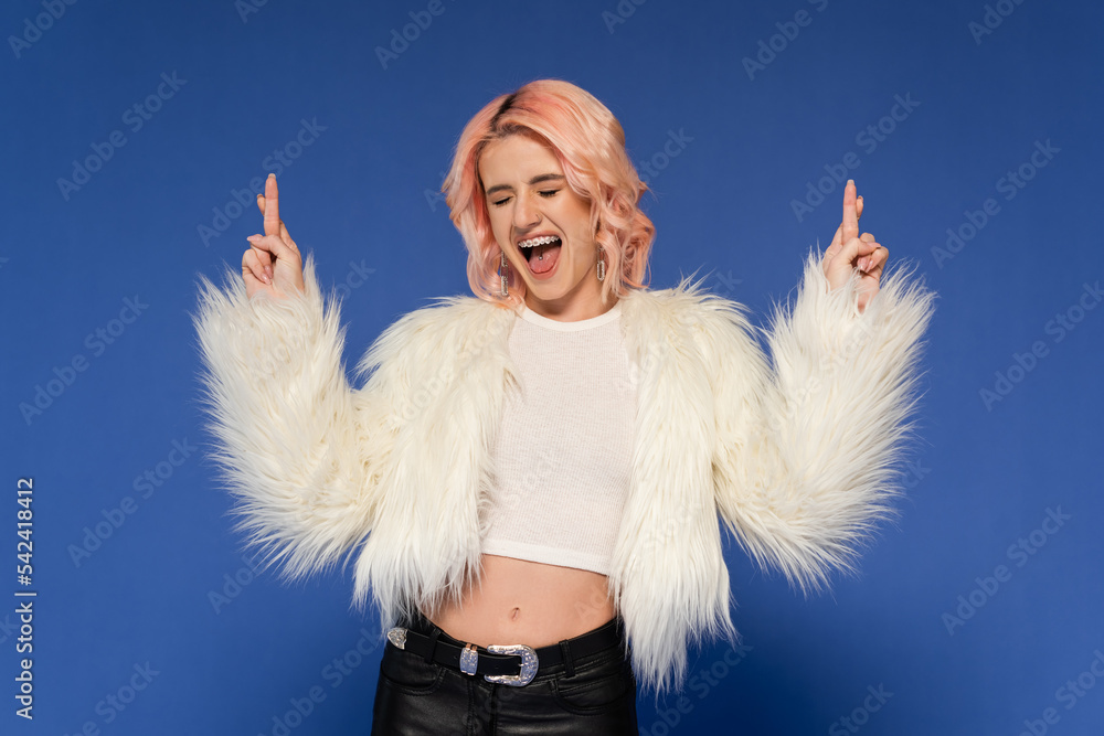 excited woman in fluffy faux fur jacket holding crossed fingers isolated on blue excited woman in fluffy faux fur jacket holding crossed fingers isolated on blue