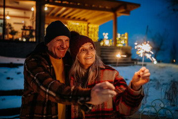 Happy senior couple celebrating new year with sparklers, enjoying winter evening.