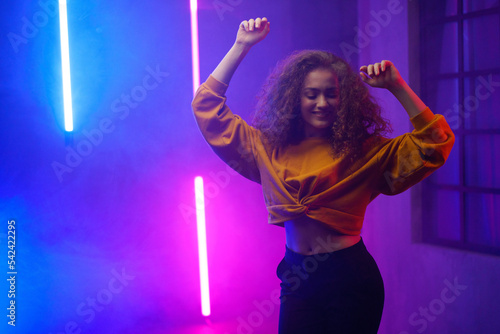Portrait of a happy young woman dancing over neon light background at disco party