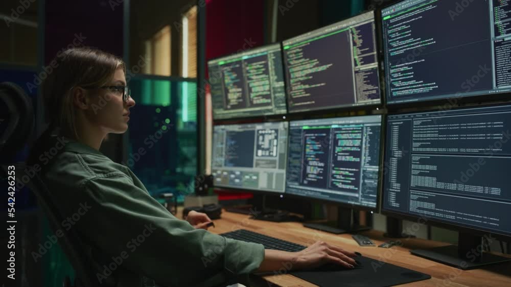 Female Cyber Security Specialist Writing Code On Deskop Computer with Six Displays in Dark Office. Caucasian Woman Controlls Digital Protection System, Monitoring Data, Debugging Software Errors. Female Cyber Security Specialist Writing Code On Deskop Computer with Six Displays in Dark Office. Caucasian Woman Controlls Digital Protection System, Monitoring Data, Debugging Software Errors.