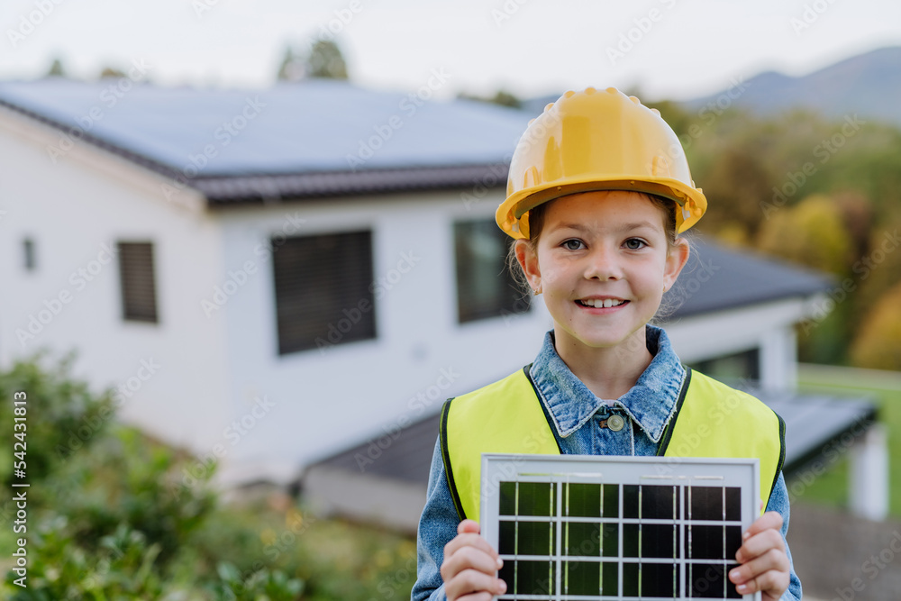 Little girl with protective helmet and reflective vest holding photovoltaics solar panel. Alternative energy, saving resources and sustainable lifestyle concept. Little girl with protective helmet and reflective vest holding photovoltaics solar panel. Alternative energy, saving resources and sustainable lifestyle concept.