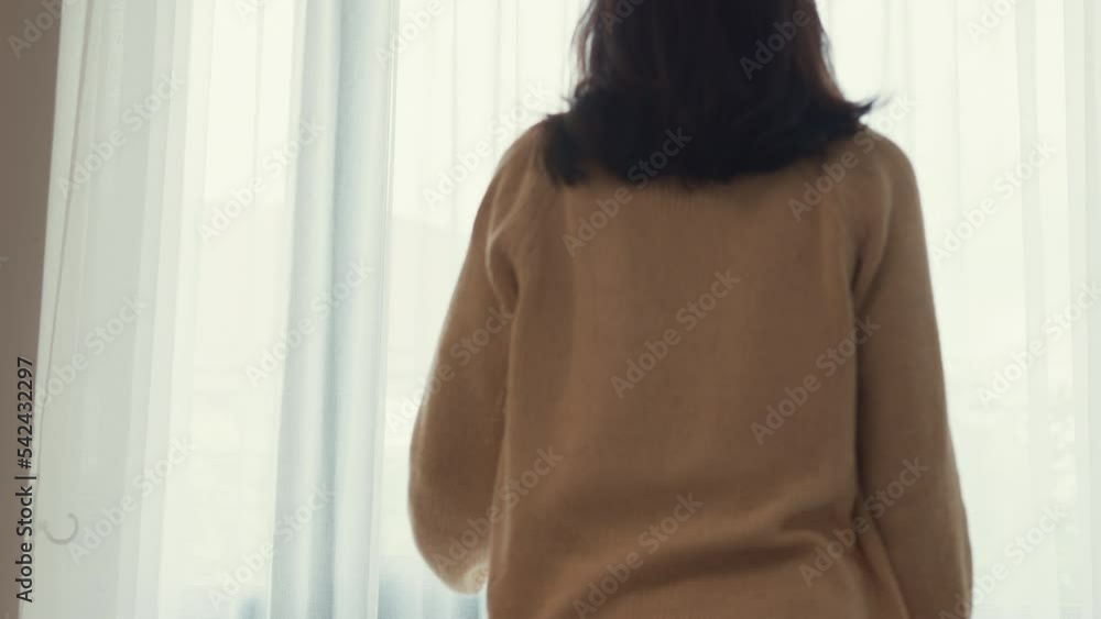 Happy Asian girl with white cream pajamas open white curtain on window looking outside feel fresh with peaceful morning and fresh air on weekend in bedroom at home. Female morning lifestyle concept.