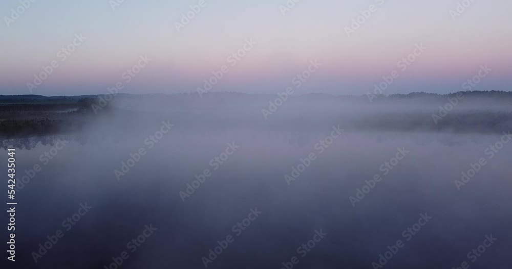 Beautiful view through bog trees during sunrise ang thick fog. Early summer morning with sunrise and birch trees. Sun shining through trees with sunbeams through woods in mystical bog swamp landscape.