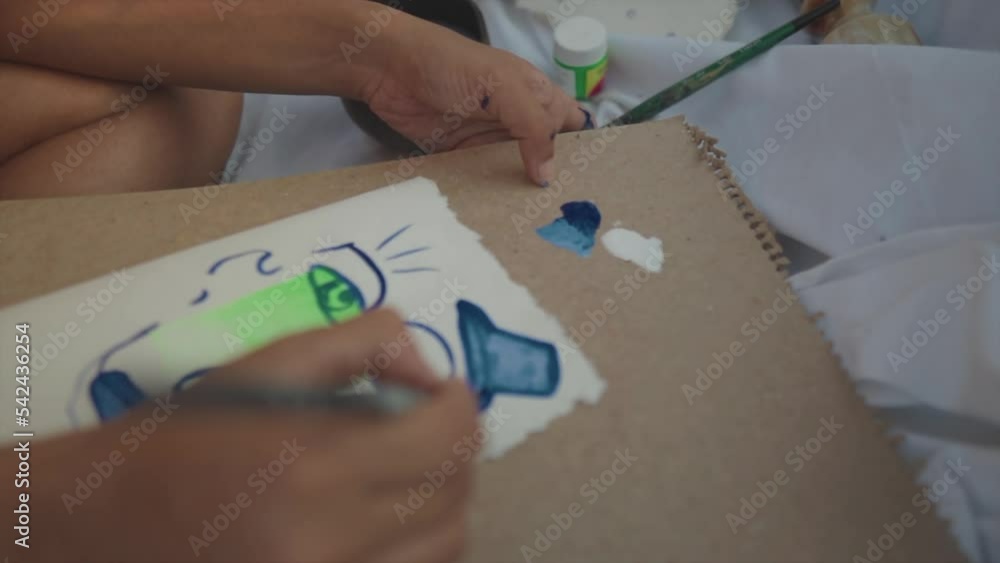 Slow motion handheld close up shot of a painting artist sitting on a white sheet painting an abstract artwork using a brush with acrylic paint Slow motion handheld close up shot of a painting artist sitting on a white sheet painting an abstract artwork using a brush with acrylic paint