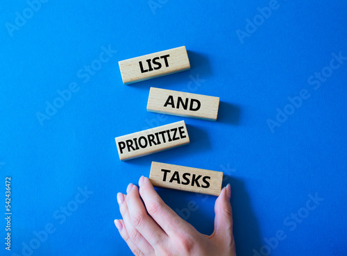 List and prioritize tasks symbol. Concept words List and prioritize tasks on wooden blocks. Beautiful blue background. Businessman hand. Business and List and prioritize tasks concept. Copy space. photo