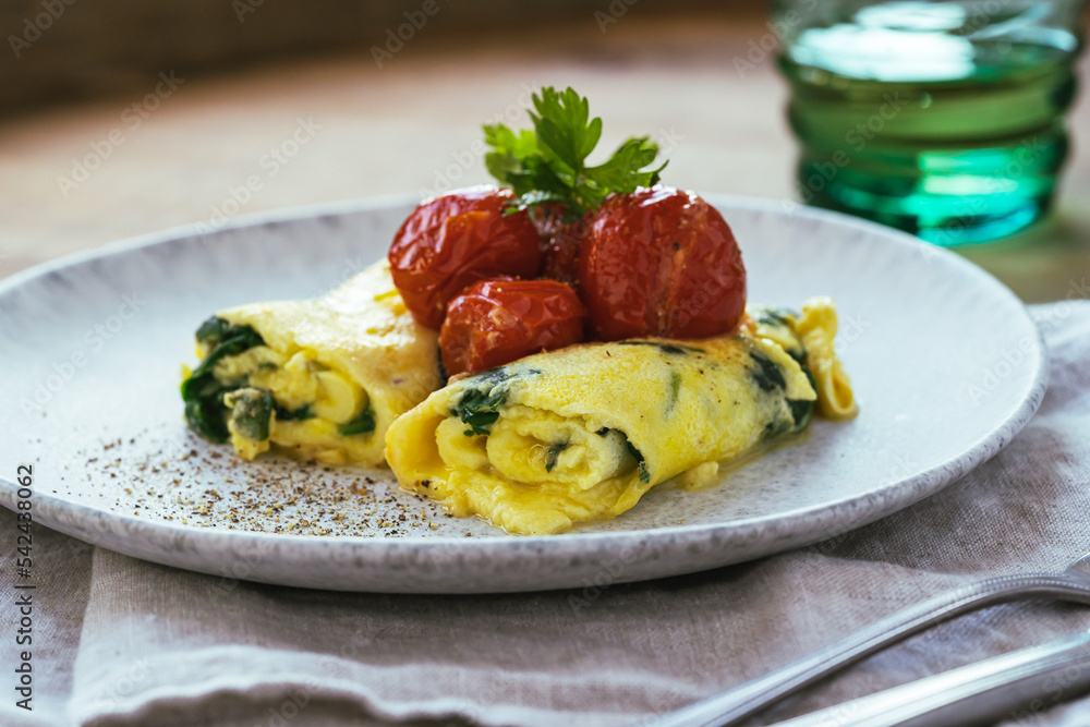 Omelet with spinach and roasted cherry tomatoes on wooden table, healthy breakfast