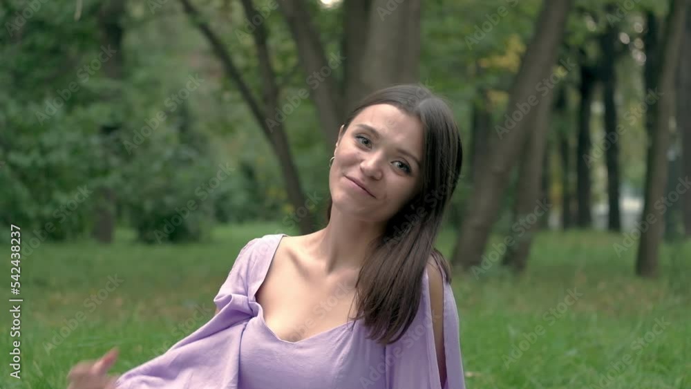 A beautiful girl in a blue dress is sitting in the park. Looks into the camera and smiles. A beautiful girl in a blue dress is sitting in the park. Looks into the camera and smiles.