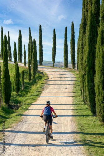 nice senior woman riding her electric mountain bike in a cypress avenue in the Chianti area near Pienza, Tuscany , Italy