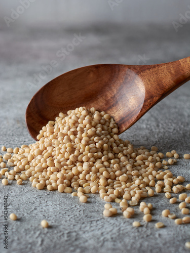 pile of organic polished white urad dal fallen from a wooden spoon, vigna mungo, also known as ulundu paruppu, or urad bean or mash kalai, on textured background with copy space, selective focus photo