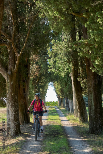 nice senior woman riding her electric mountain bike in an old oak tree avenue in the Casentino area near Arezzo,Tuscany , Italy 