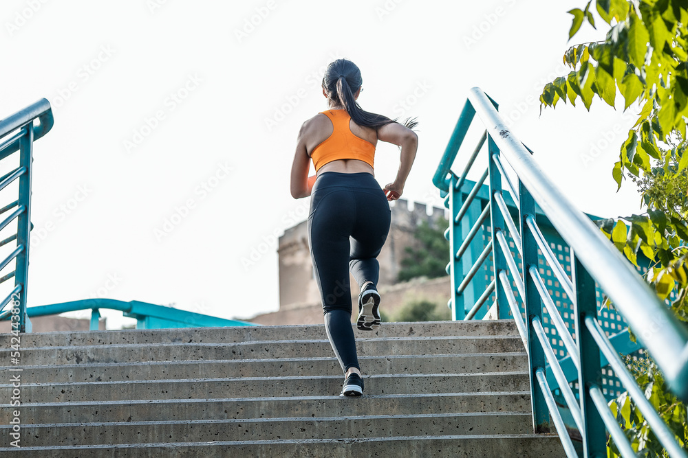 Sporty young woman in sportswear running up stairs in the city.