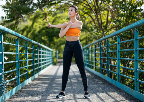 Young sporty woman listening to music with earphones while stretching over a bridge.