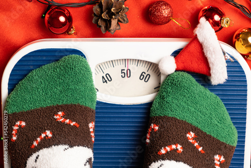 фотографія A woman in Christmas socks stands on the scales, weighs herself after gluttony d