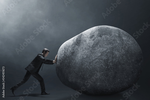 Business man pushing big stone on dark background