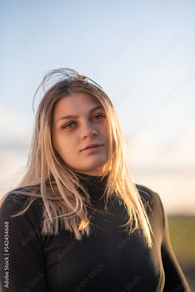 Portrait of a young beautiful blonde girl in a black turtleneck at sunset.