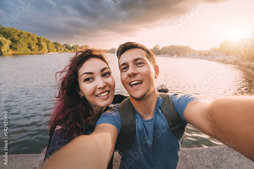 A couple in love or just friends students takes a selfie photo with scenic sunset lake view in city park. Vacation, education and relationship concept