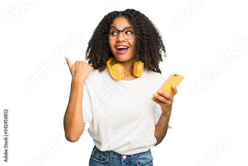Foto Young african american woman listening to music with yellow headphones isolated points with thumb finger away, laughing and carefree