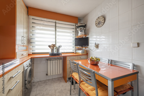 Fototapeta Naklejka Na Ścianę i Meble -  Corner of a conventional kitchen with bright orange cabinets combined with beech wood and a rectangular table with matching chairs