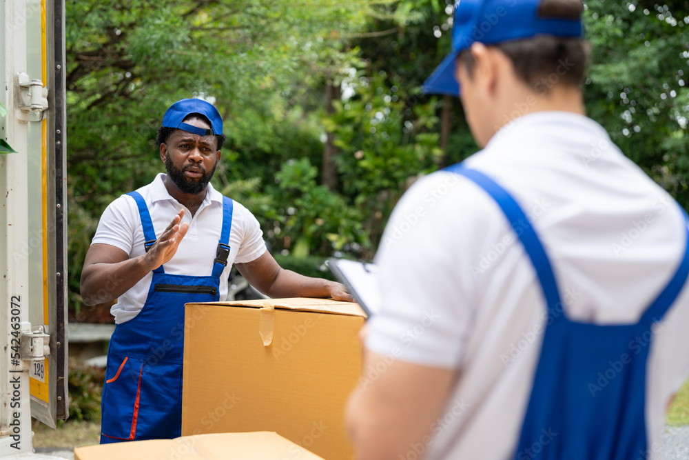 Man mover worker in blue uniform checking lists on clipboard while unloading cardboard boxes from truck.Professional delivery and moving service. Man mover worker in blue uniform checking lists on clipboard while unloading cardboard boxes from truck.Professional delivery and moving service.