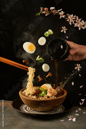 Chef pouring miso broth into bowl with ramen in studio photo