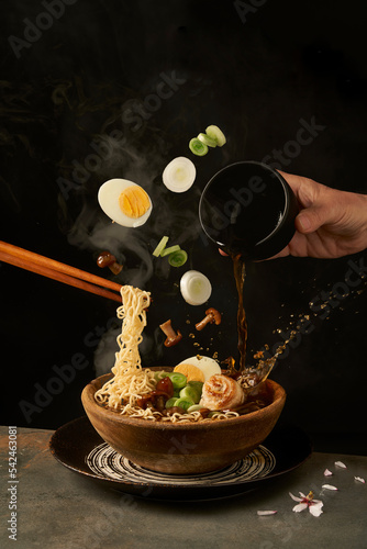 Chef pouring miso broth into bowl with ramen in studio