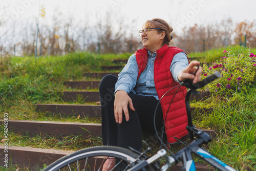 Middle aged smiling mature woman holdingt a bike with her hands on the grass on a green field. Summer or Autumn Country Vacation and Adventure Concept