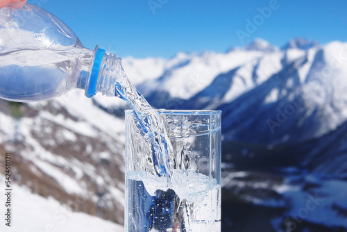 Pouring water from bottle into a glass on a background of winter landscape of mountains. Healthcare hydration concept