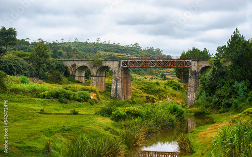 Small railway bridge over small river near Manjakandriana, Madagascar, green grass and trees around. There is only small number of railroads on whole island