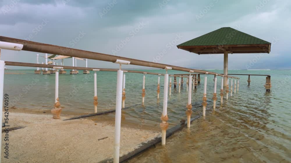 Calm morning at Ein Bokek Dead Sea beach, steel rails leading to sun shade shelter
