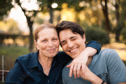 Happy mature mother hugging smiling adult son in park in summer