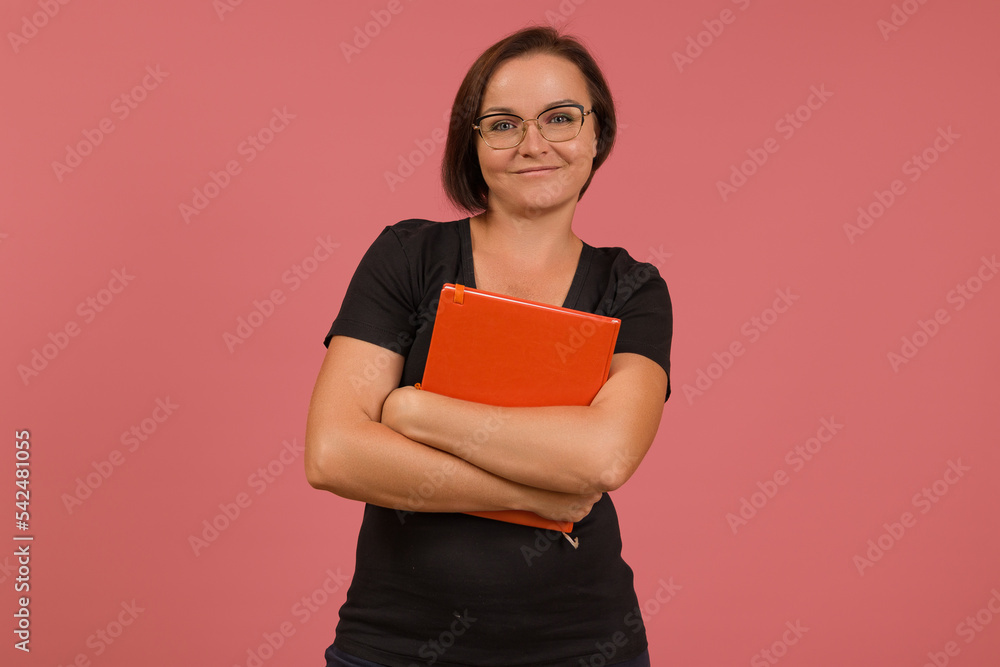 cute female teacher with a pleasant expression smiling at the camera holding a notebook in her arms cute female teacher with a pleasant expression smiling at the camera holding a notebook in her arms
