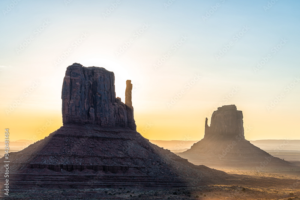 Closeup of east and west mitten buttes and horizon in Monument Valley at sunrise colorful light and sun beam rays behind rock formations in Arizona