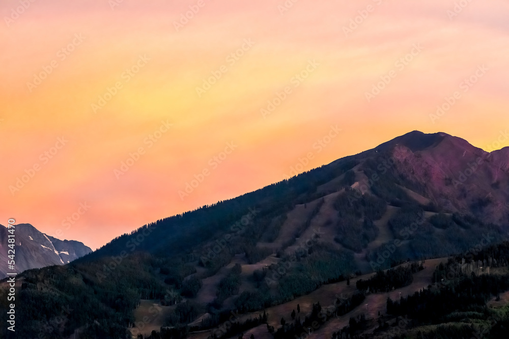 Pastel orange sunset in Aspen, Colorado with rocky mountains peak in autumn and vibrant yellow color at twilight over buttermilk ski resort