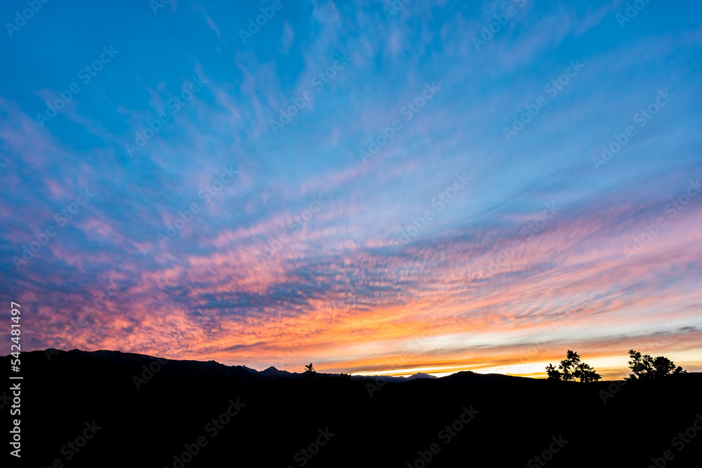 Aspen, Colorado rocky mountains silhouette of ridge and Capitol peak and vibrant color of sunset orange light in blue sky wide angle view of skyscape