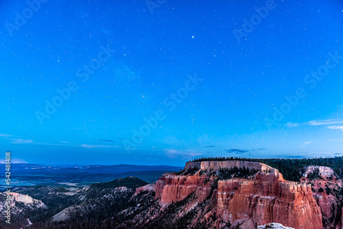 Night sky with stars in milky way in Bryce Canyon National Park in Utah showing red canyons landscape and vibrant blue color at Paria view overlook at twilight
