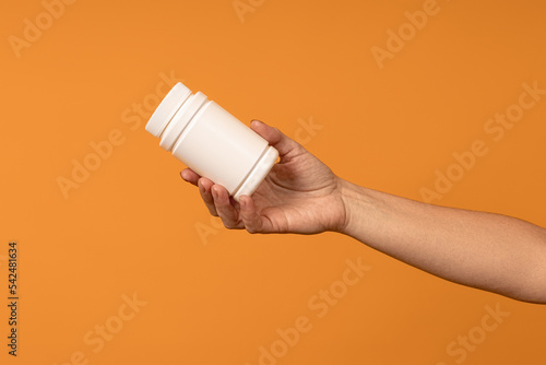 female hand holds out a bottle of pills on a yellow background