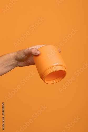upside down empty yellow bottle in hand on orange background