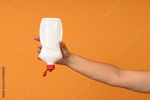 upside down white plastic bottle with open red cap in hand on yellow background
