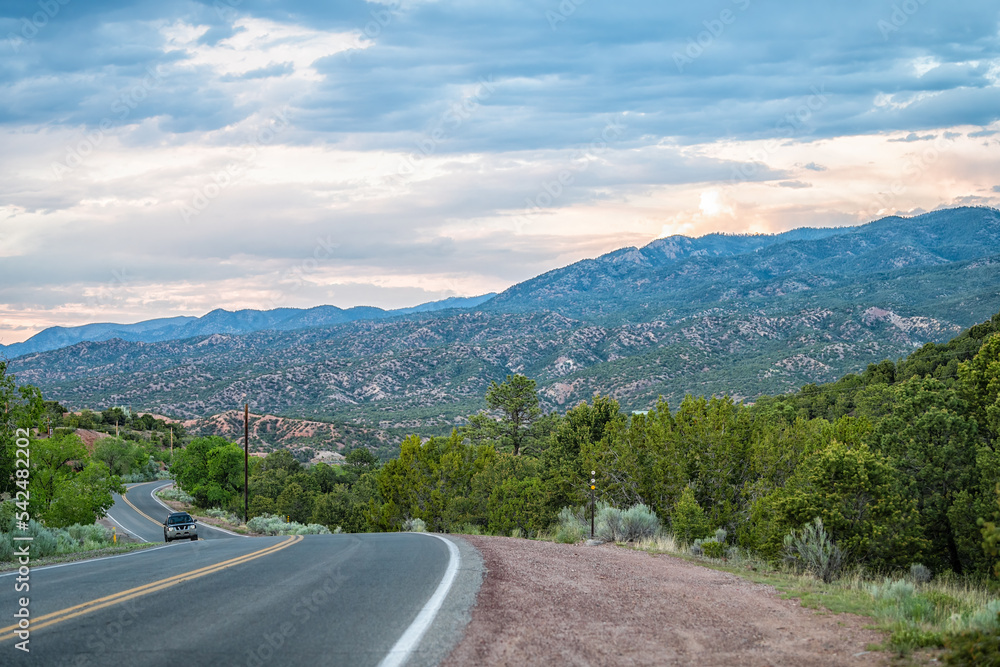 Naklejka premium Sangre De Cristo mountains sunset on Bishops Lodge Road street in Santa Fe New Mexico with car driving, pink sunlight by Tesuque residential community