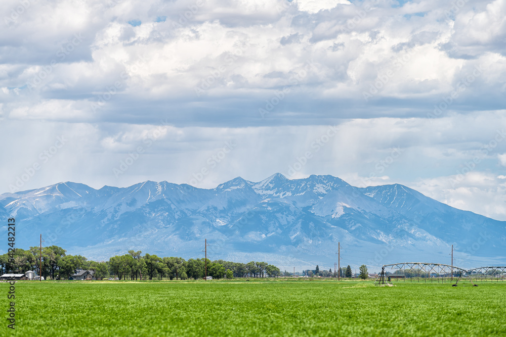 Monte Vista, Colorado countryside in summer on cloudy day with green grass and mountain view by farm equipment irrigation water system for watering crop harvest plants