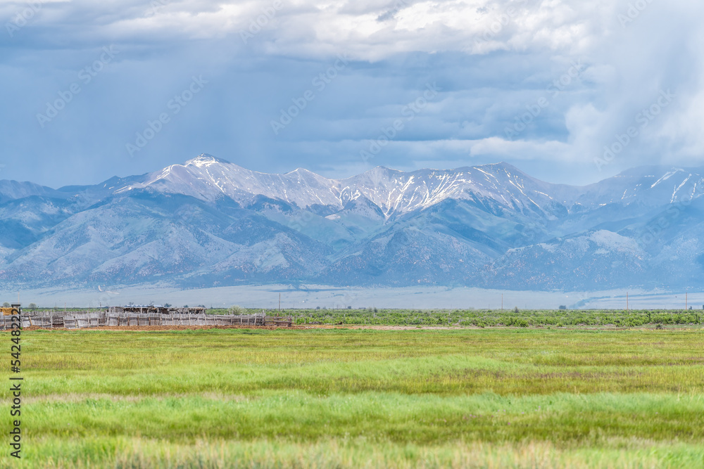Colorado route 285 with rural farm pasture field near Center and Monte Vista with view of Rocky Mountains by industrial agricultural shed barn stables