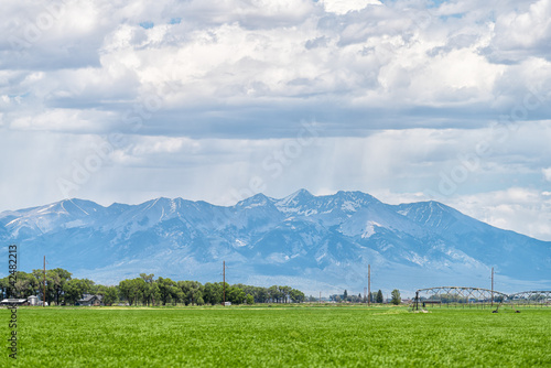 Monte Vista, Colorado countryside in summer on cloudy day with green grass and mountain view by farm equipment irrigation water system for watering crop harvest plants photo
