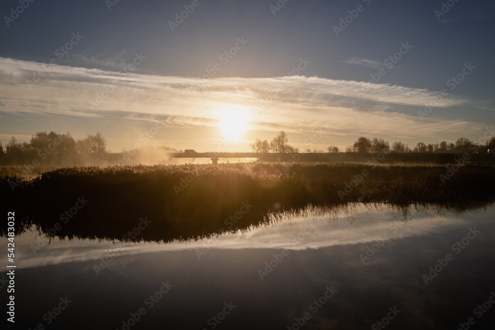 morning mist covers river and bridge at sunrise, symmetric reflection of clouds